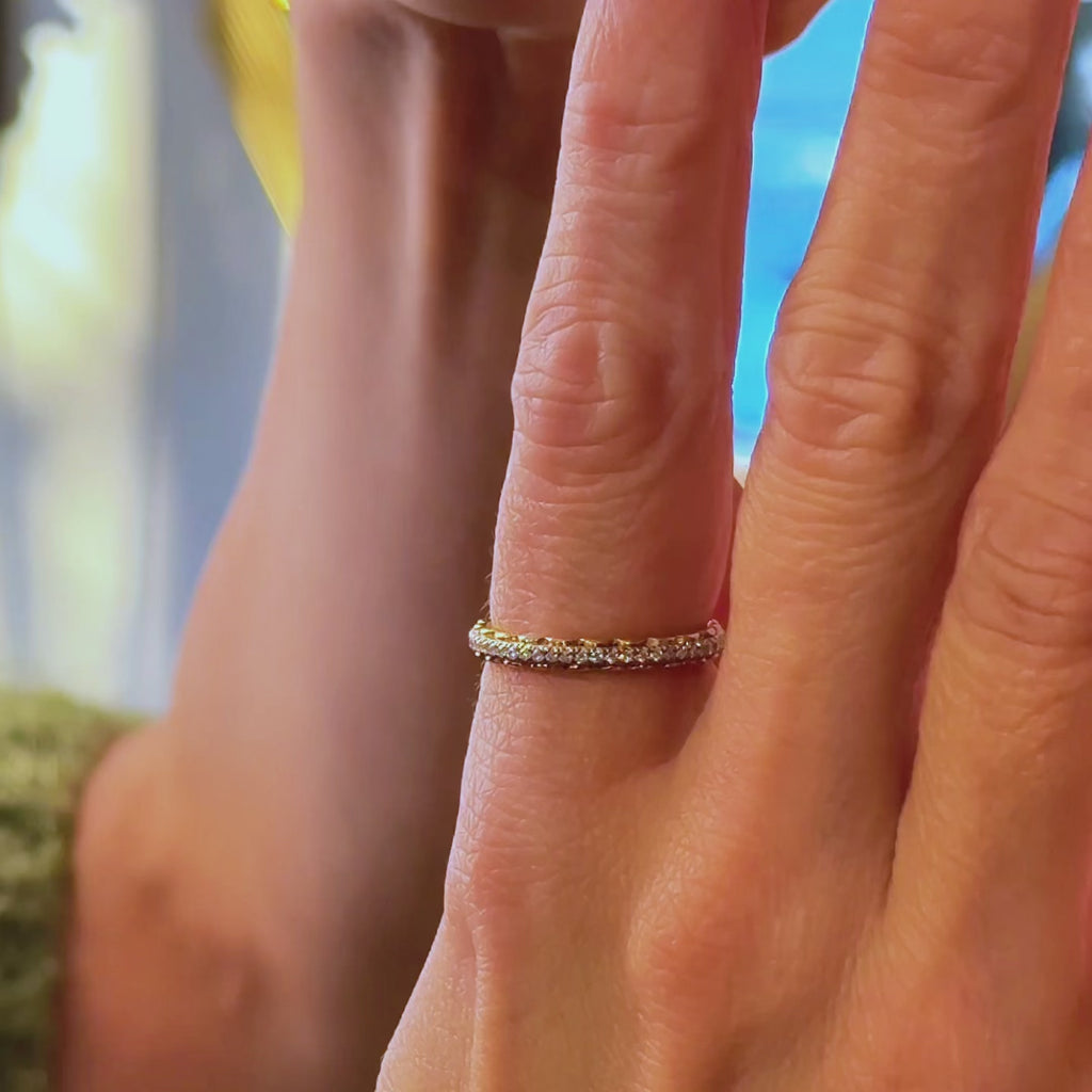 A video showcasing a hand adorned with a beautifully stacked set of rings. At the center is a 14k yellow gold double-row diamond eternity band, sparkling brilliantly under soft lighting. It is paired with a solitaire malaya garnet ring, its warm peach-pink hue complementing the diamonds, and flanked by two other wedding bands. The combination creates a stunning, layered look, highlighting the elegance and versatility of the rings when worn together. The hand moves gently to showcase the sparkle and texture 