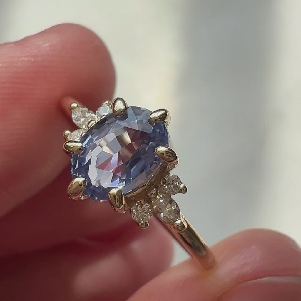 Close-up video of light blue sapphire and diamond engagement ring in 14k yellow gold, worn on hand. Handmade by Maksym Jewelry, available at Ruby Mardi, Montreal.