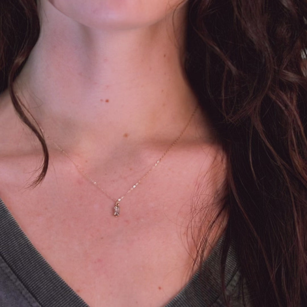 Video featuring a young woman with long, wavy hair modeling a delicate 18-inch gold chain necklace adorned with a marquise-shaped salt & pepper diamond pendant. The video captures the diamond's stunning sparkle under the light, highlighting its clarity, while the colorful, festive background enhances the lively atmosphere of Ruby Mardi.