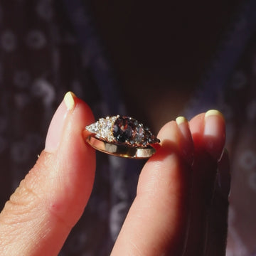 Close-up video of a yellow gold engagement ring featuring an oval plum sapphire, marquise and pear-shaped diamonds, and brilliant-cut diamond accents sparkling in natural sunlight as the ring gently moves.
