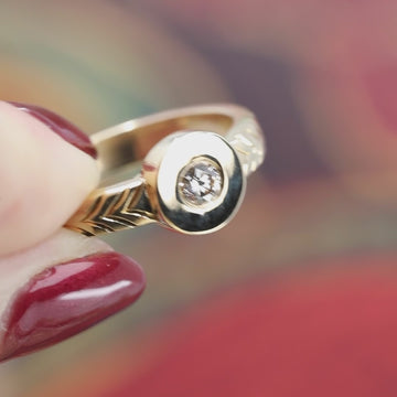 A short video with a jazz music presenting in close up a think gold designer ring. The wedding band has beautiful hand engraved details. It also shows a bold central round gold plate in which is set a round natural diamond color champagne.