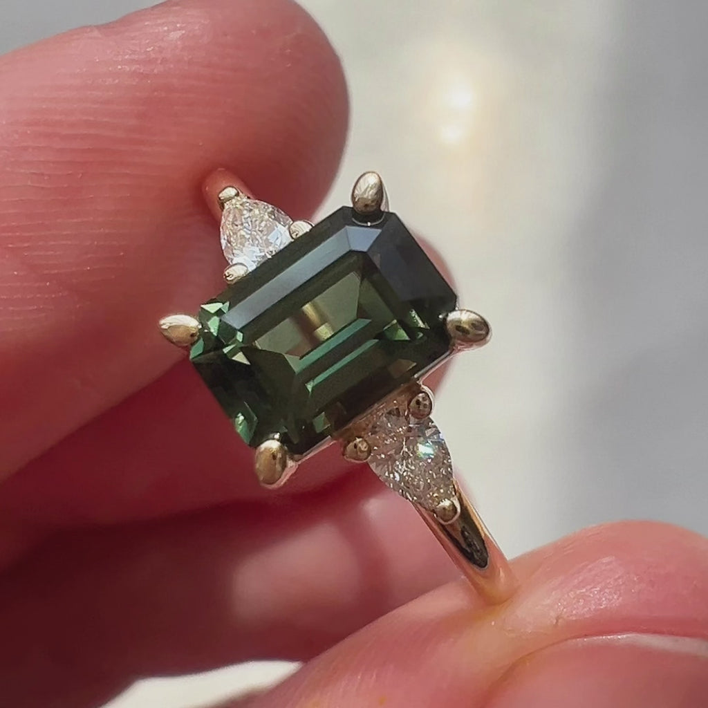 Video of an alternative engagement ring featuring an emerald-cut green sapphire flanked by pear-shaped natural diamond accents. The close-up highlights the clean lines, rich green tones, and graceful sparkle of the design.