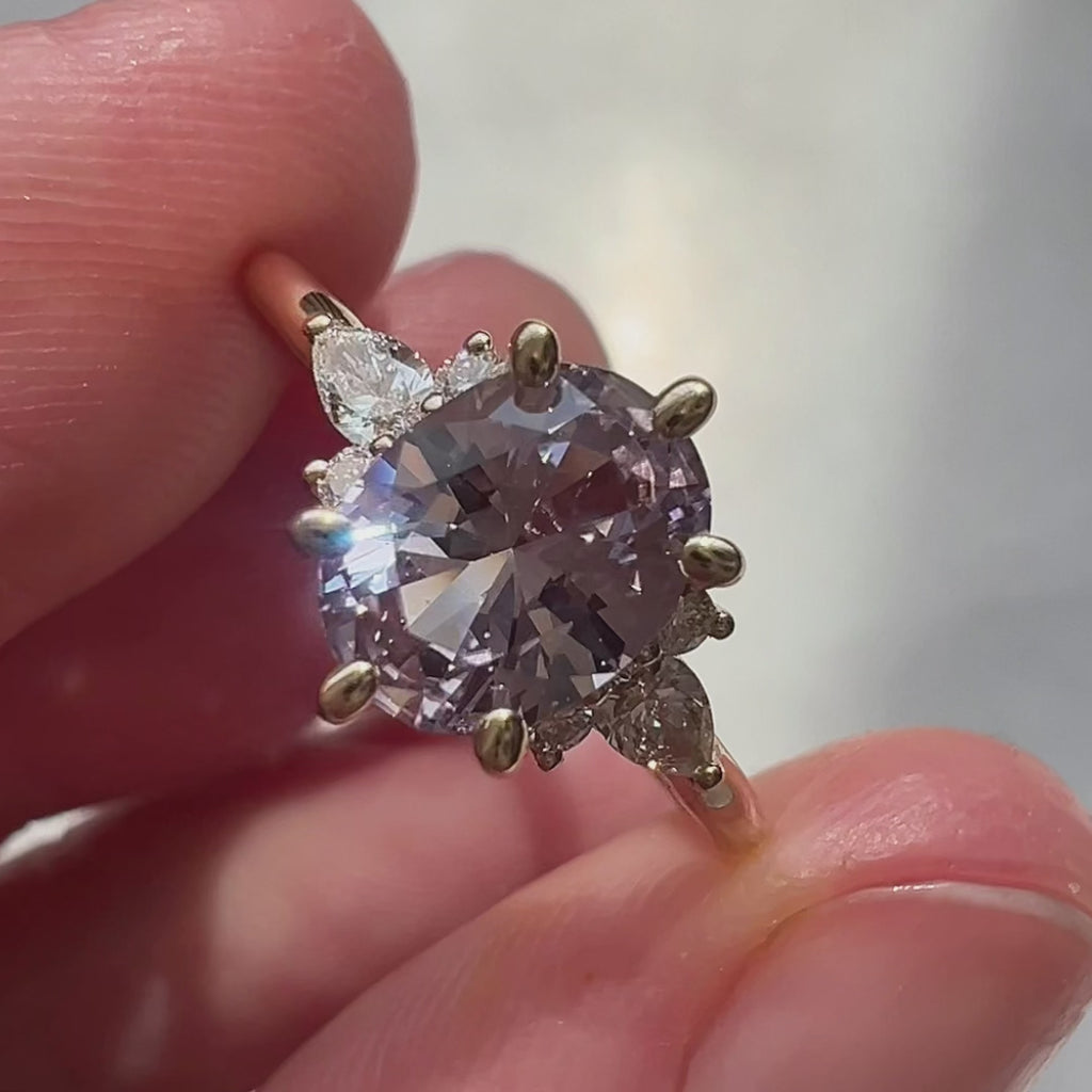 Close-up video of a lilac sapphire engagement ring with diamond accents in 14k yellow gold, handmade by Maksym Jewelry and shown worn on the hand. Filmed in natural light to highlight the gem’s soft purple hue and refined sparkle. Ruby Mardi, Montreal.