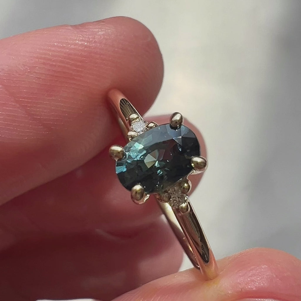 Video of a deep teal sapphire engagement ring shown in close-up and worn. The gemstone’s rich, moody hues shimmer as the light moves, revealing the ring’s elegant setting and timeless silhouette.