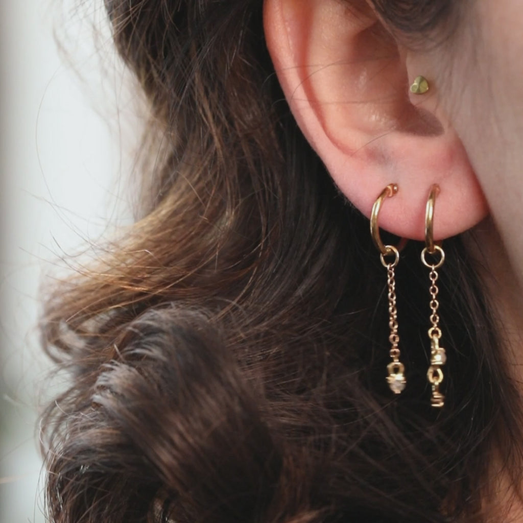 Video showing asymmetrical 10k yellow gold hoop earrings by Nadia Werchola worn on the ear, with dangling rose-cut grey and white diamonds moving gently to show their sparkle, available at Ruby Mardi in Montreal.