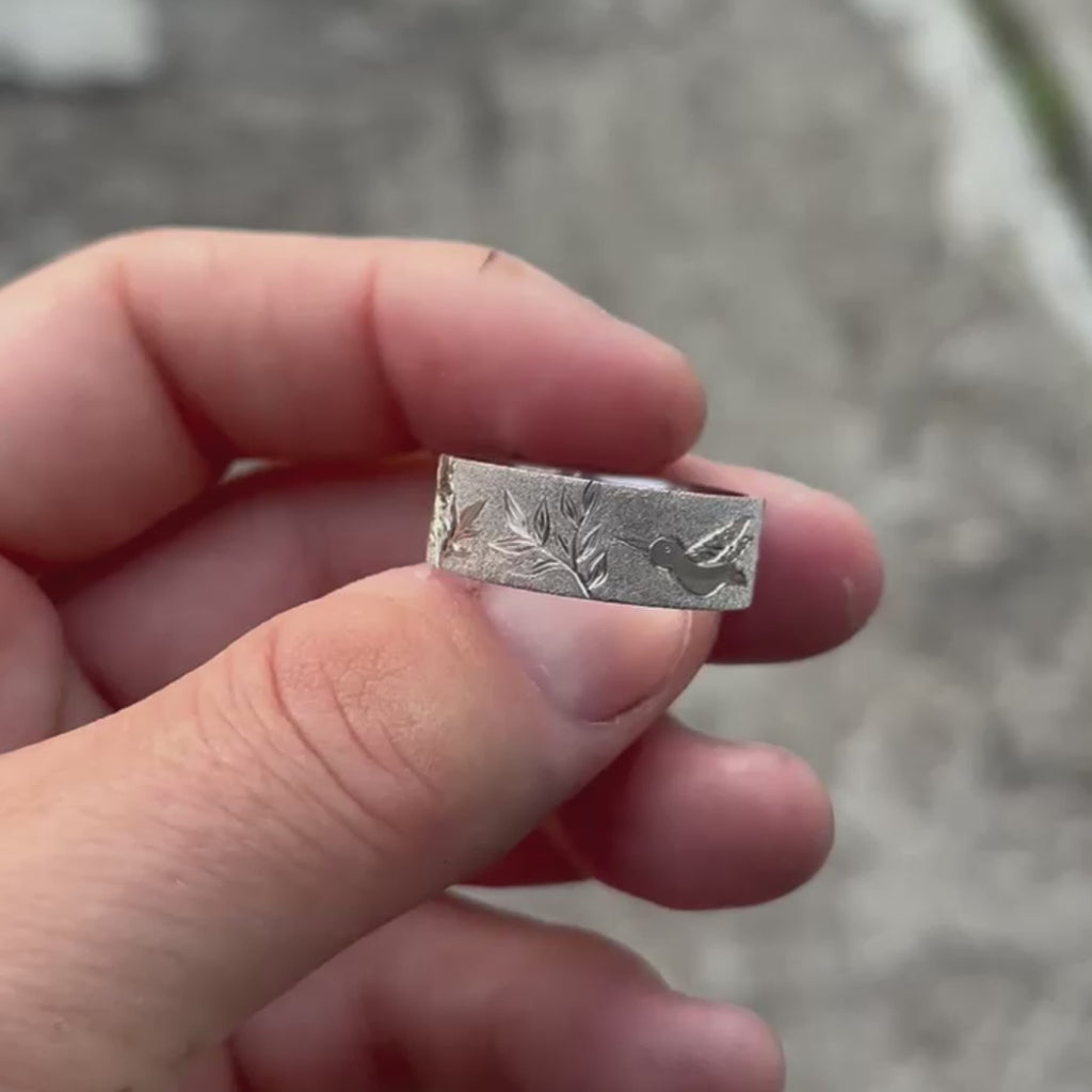 Video of a hand-engraved white gold band held in the jeweller’s work-worn hands, showing the pencil-drawn floral design before engraving. The close-up captures the authentic, artisanal nature of the process, with visible bench dust and tool marks that highlight the craft behind Rebel & Rogue’s engraving work.
