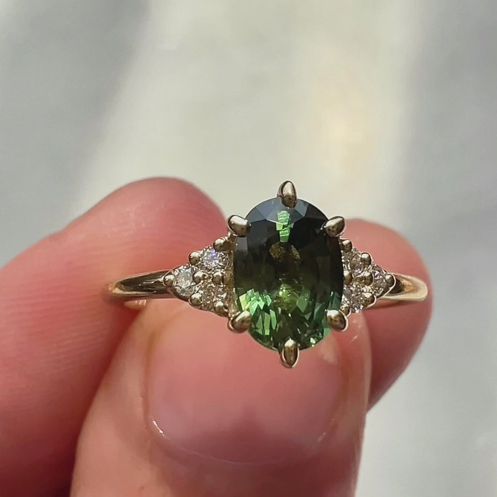 Close-up video of a yellow gold ring featuring an oval green sapphire center stone and small white diamonds on each side, sparkling under natural light.