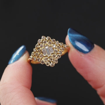 Close-up video of a lace-inspired diamond ring in yellow gold, featuring a delicate cluster of champagne diamonds surrounding three vertical baguette-cut white diamonds at the center, creating an intricate, airy texture with warm tones and refined sparkle.