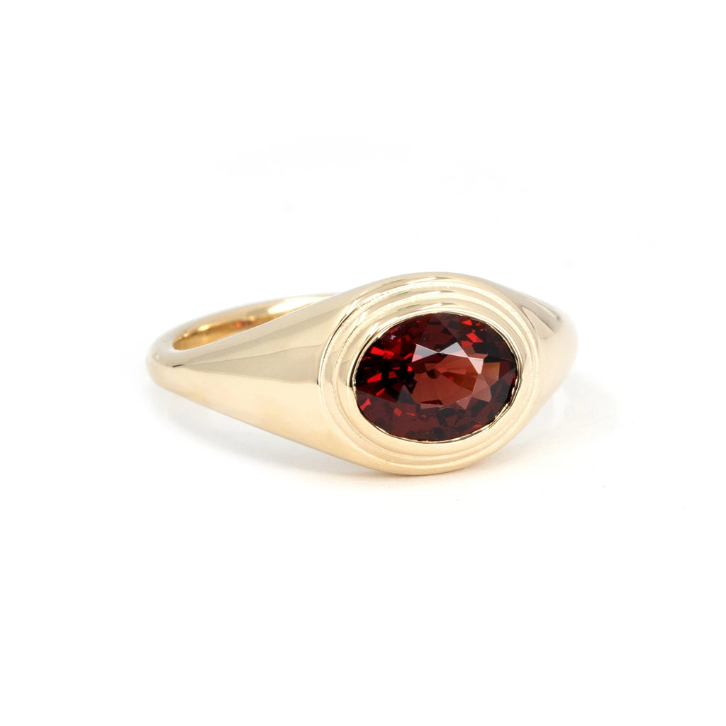 Yellow gold statement ring featuring an oval rose-cut deep red pyrope garnet in a sleek bezel setting, photographed on a white background.