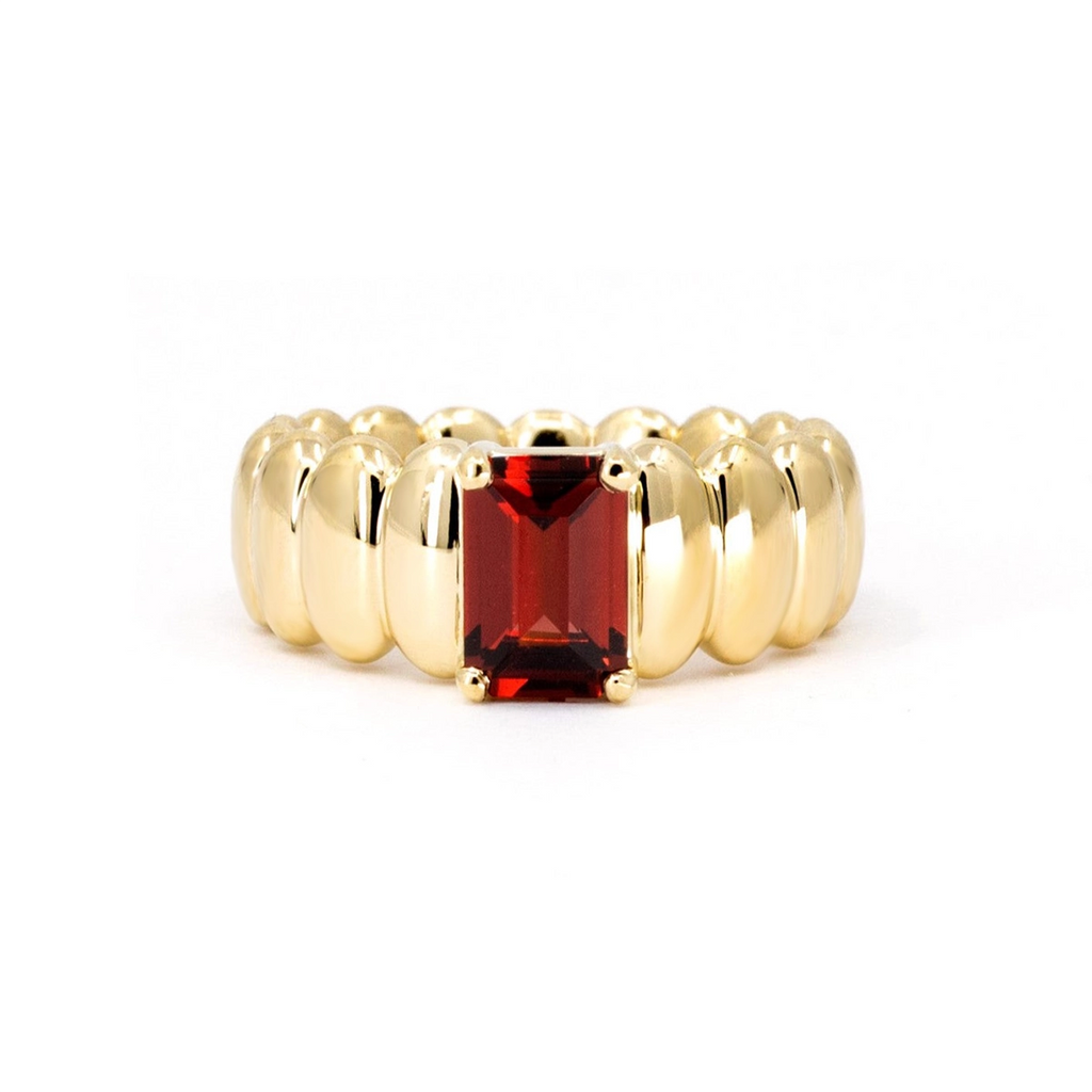 Bold yellow gold ring featuring a band made of elongated, rounded shapes, with a rectangular pyrope garnet in the center. This fashion ring with a dark red gemstone is made in Canada by the independent Bena Jewelry brand. This ring can be custom-ordered with your favorite stone. Shown here photographed against a white background.