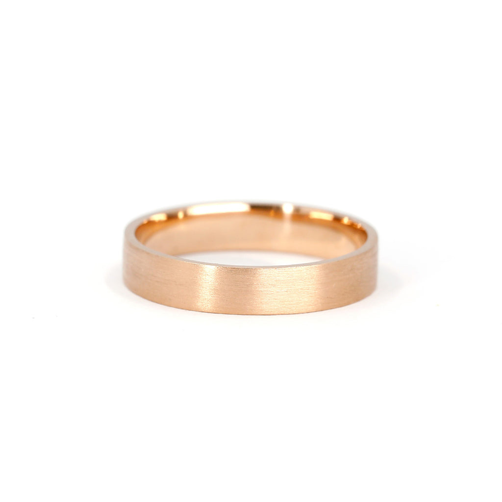 Product photography of a rose gold wedding band with a satin matte finish. 