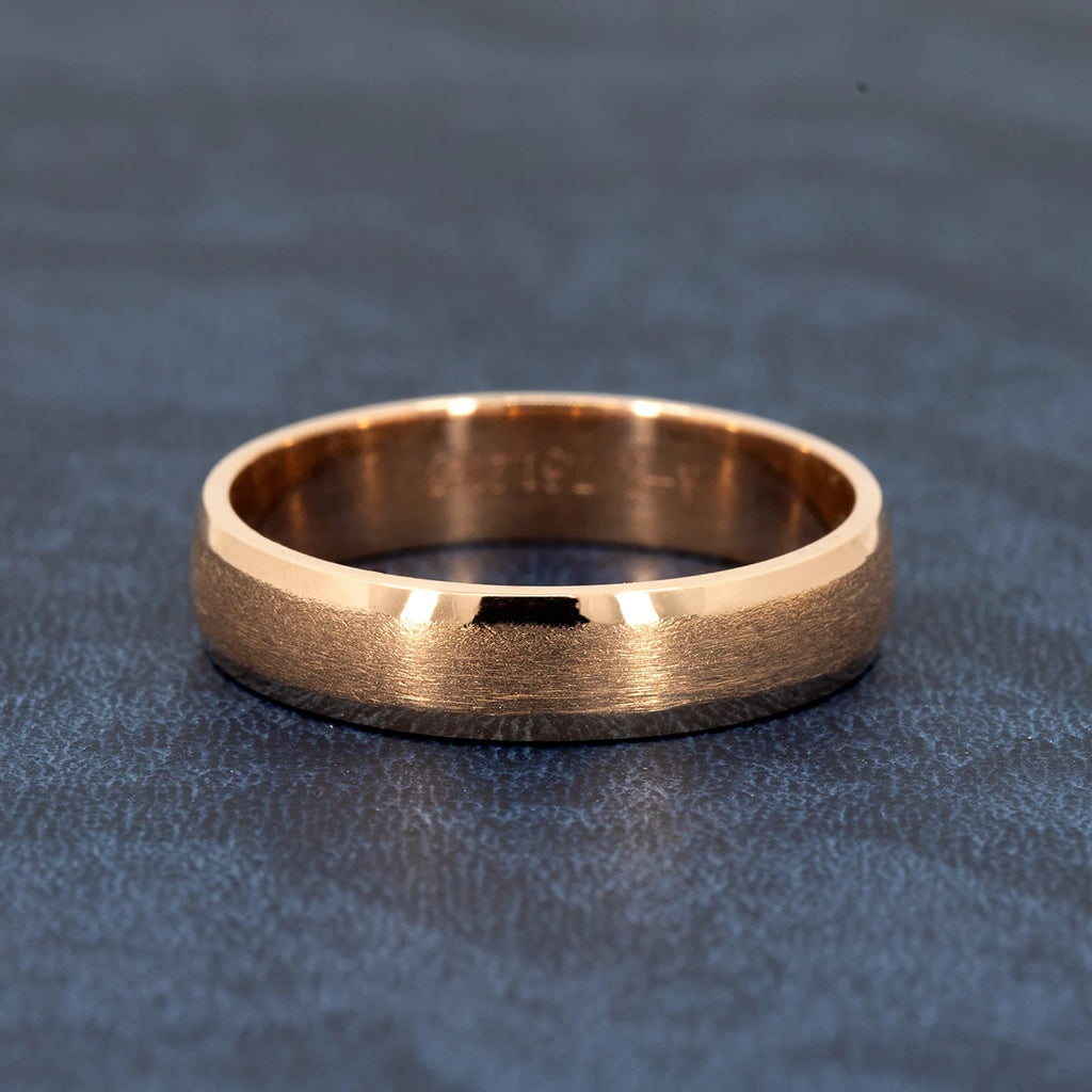 Unisex 5.5mm rose gold wedding band with rounded edges and matte center, handmade by Ruby Mardi Jewelry, displayed on dark blue leather.