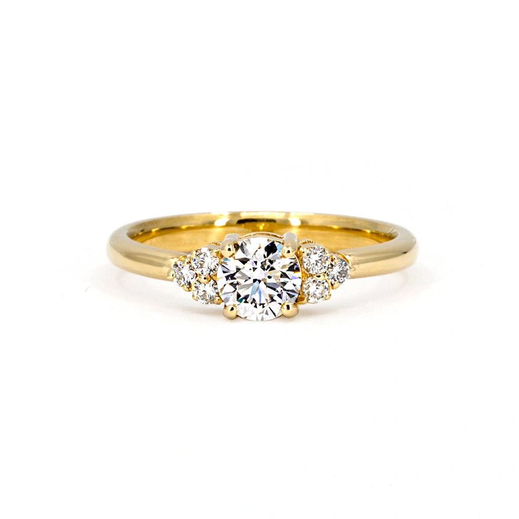 Classic diamond engagement ring handmade in Canada by independent jewelry brand Ruby Mardi. This bridal ring is made of yellow gold and features a central round brilliant diamond as well as 6 small diamond accents. We offer the best jewelry in Canada.