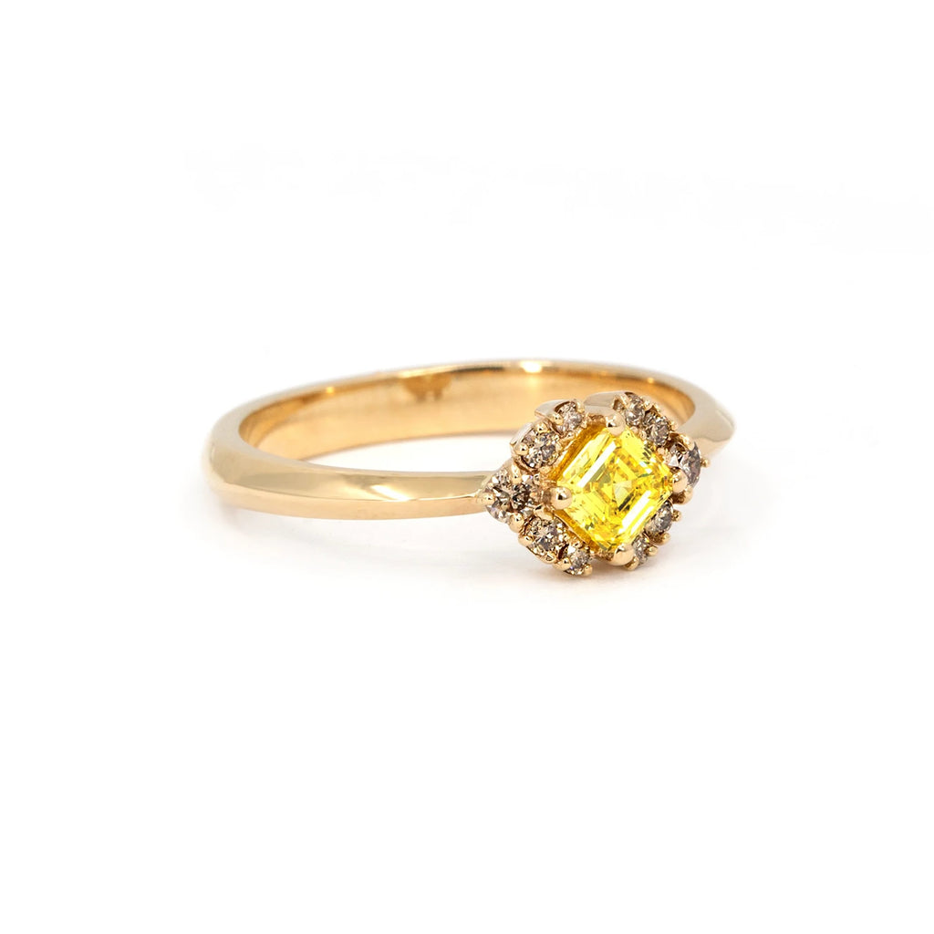 Yellow gold ring with a central asscher-cut yellow diamond, accented by champagne diamonds on each side, displayed against a white background.