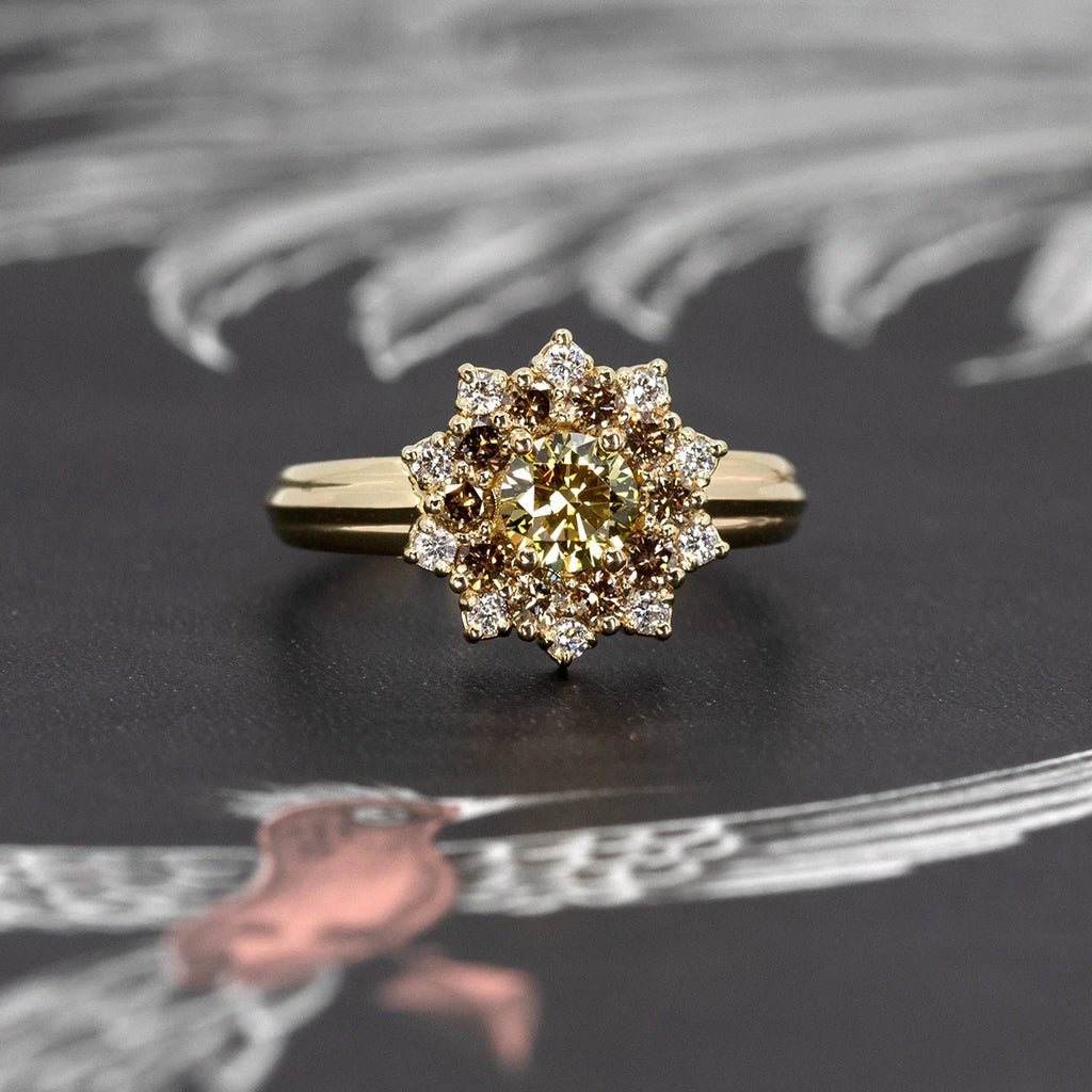 Front view product image of a sun-shaped ring showcased against a dark illustration featuring a pink bird. The ring features a broad yellow gold band with a central round yellow laboratory diamond, encircled by round gold/brown diamonds and radiant white diamonds. This unique alternative engagement ring is designed by independent fine jewelry designer Bena Jewelry, highlighting exceptional craftsmanship.