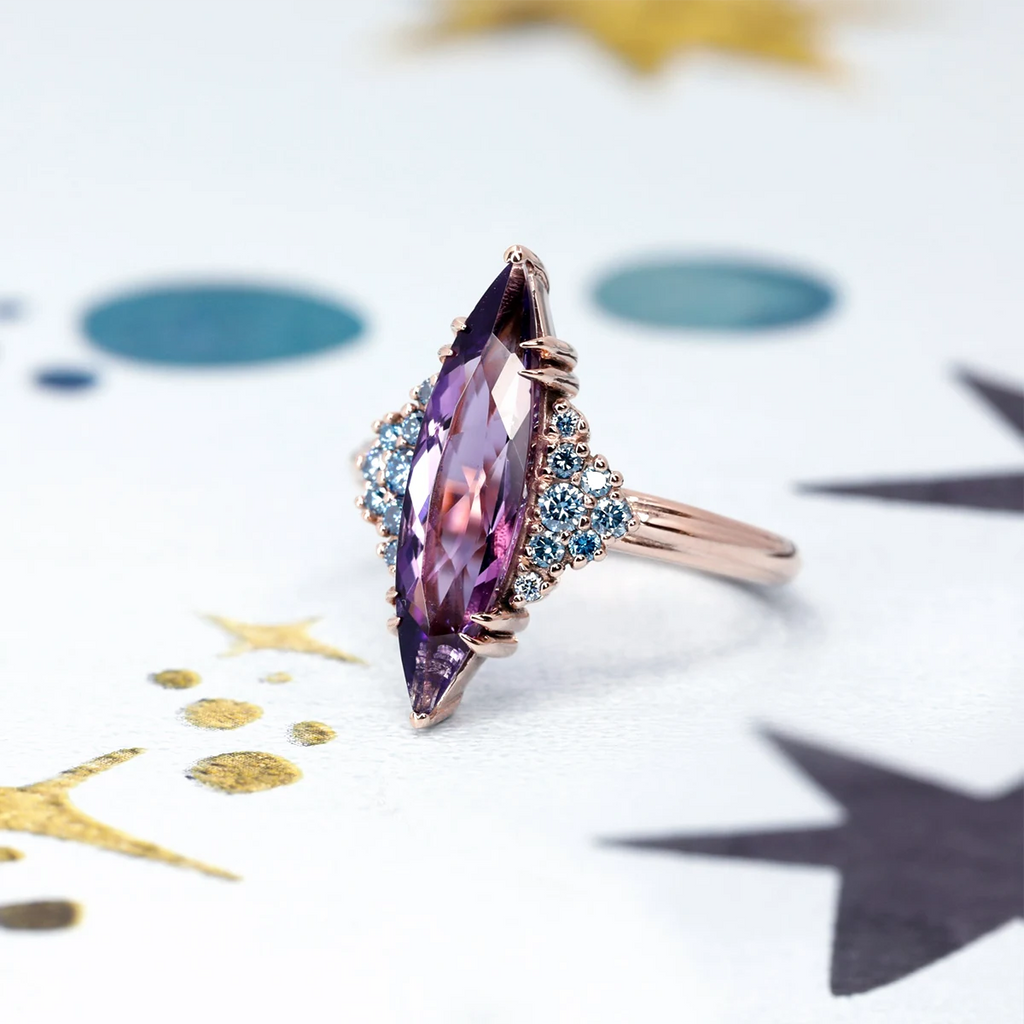 Large marquise-cut amethyst ring with clusters of blue diamond accents in rose gold, displayed on a starry background – Bena Jewelry, Ruby Mardi Montreal.