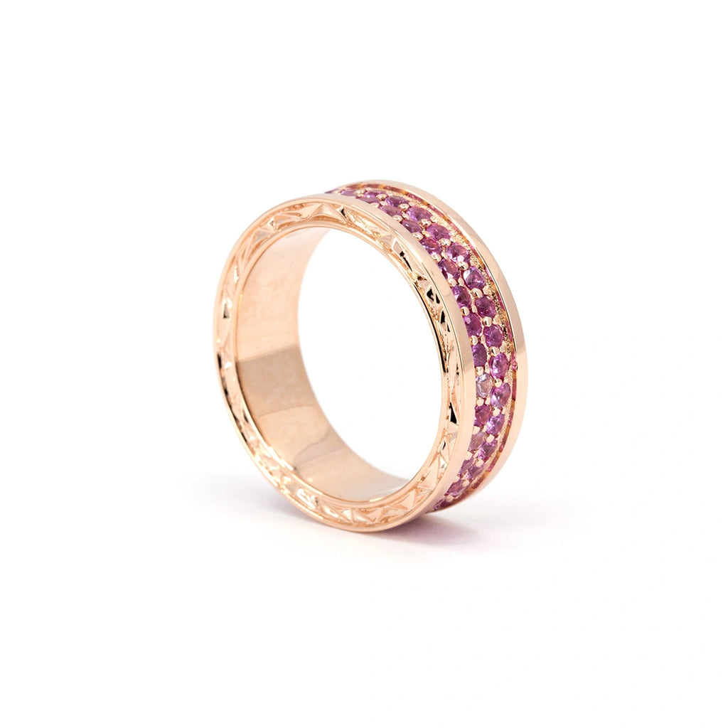 Rose gold ring featuring two rows of vivid pink sapphires pavé-set in the center channel, framed by polished hand-engraved edges with chiseled detailing. This bold and refined design by Bena Jewelry is handcrafted in Montreal and available at Ruby Mardi. A modern statement band blending precision, color, and artistry.
