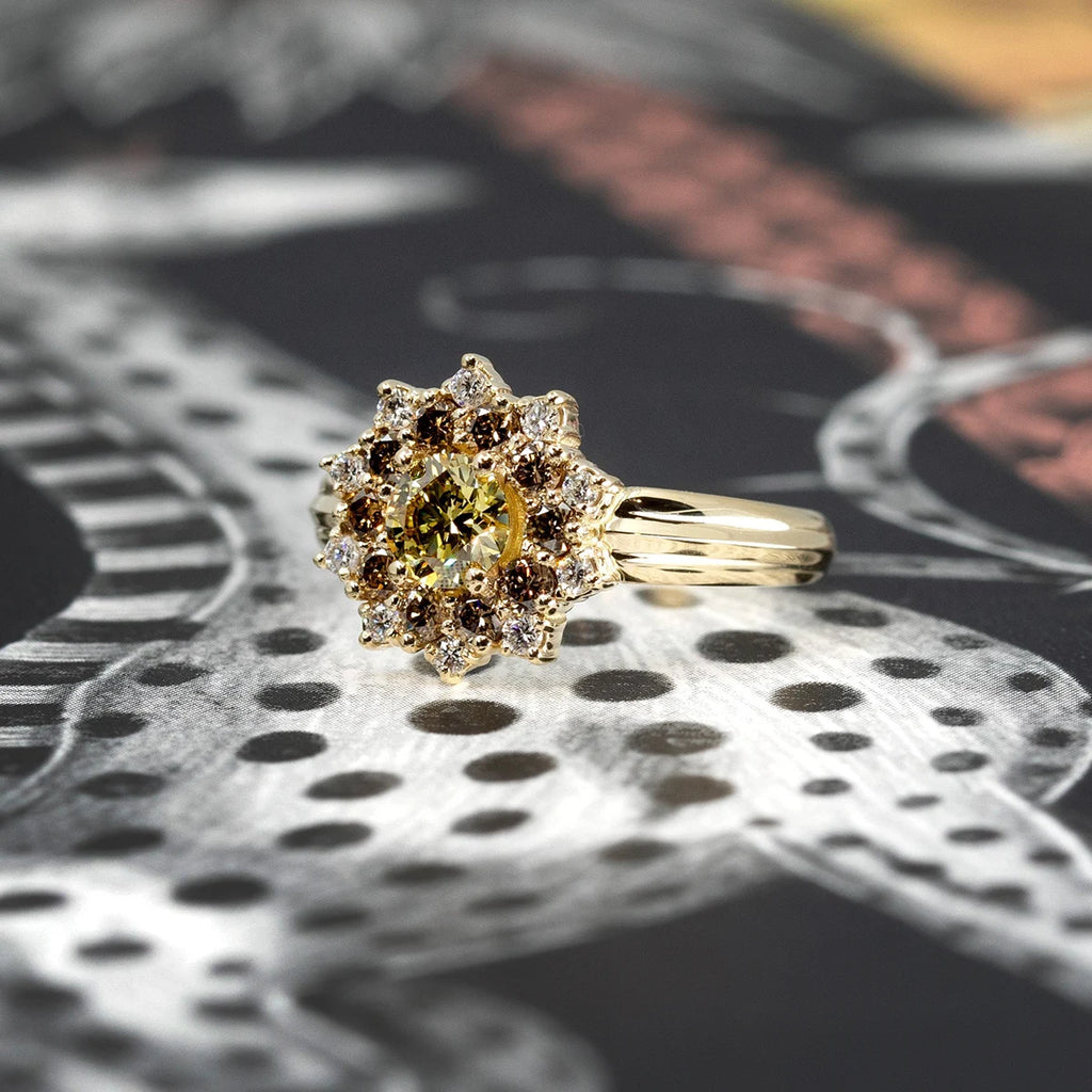 Product photo of a sunburst ring viewed from the side, displayed on a dark background featuring a polka-dot giraffe. The ring showcases a wide yellow gold band with a central round yellow laboratory diamond, surrounded by round gold/brown diamonds and white diamonds. This distinctive alternative engagement ring is a creation of independent fine jewelry designer Bena Jewelry.