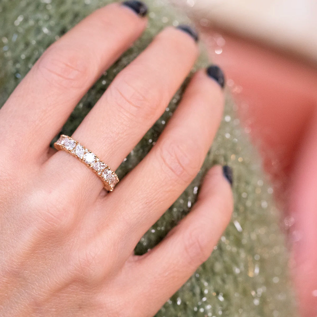 Hand wearing a yellow gold diamond eternity band, featuring a continuous row of round brilliant diamonds. The ring is shown in natural lighting, highlighting the sparkle of the stones.