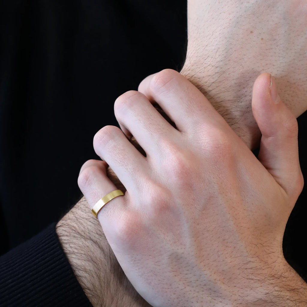 Close up on a man wearing a black sweater and a satin matte yellow gold wedding ring. This classic band was handmade in Montreal by independent brand and jewelry store Ruby Mardi.