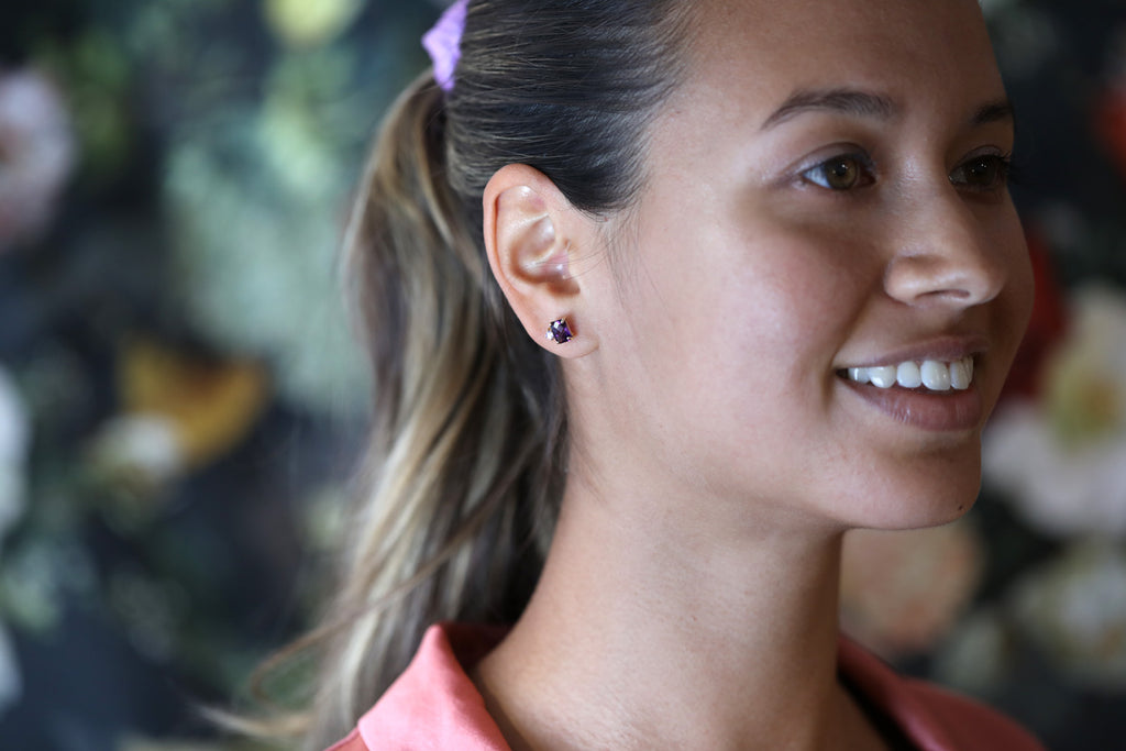 A young smiling lady wears a high end earring handmade from 18k yellow gold, pink sapphire and amethyst. 