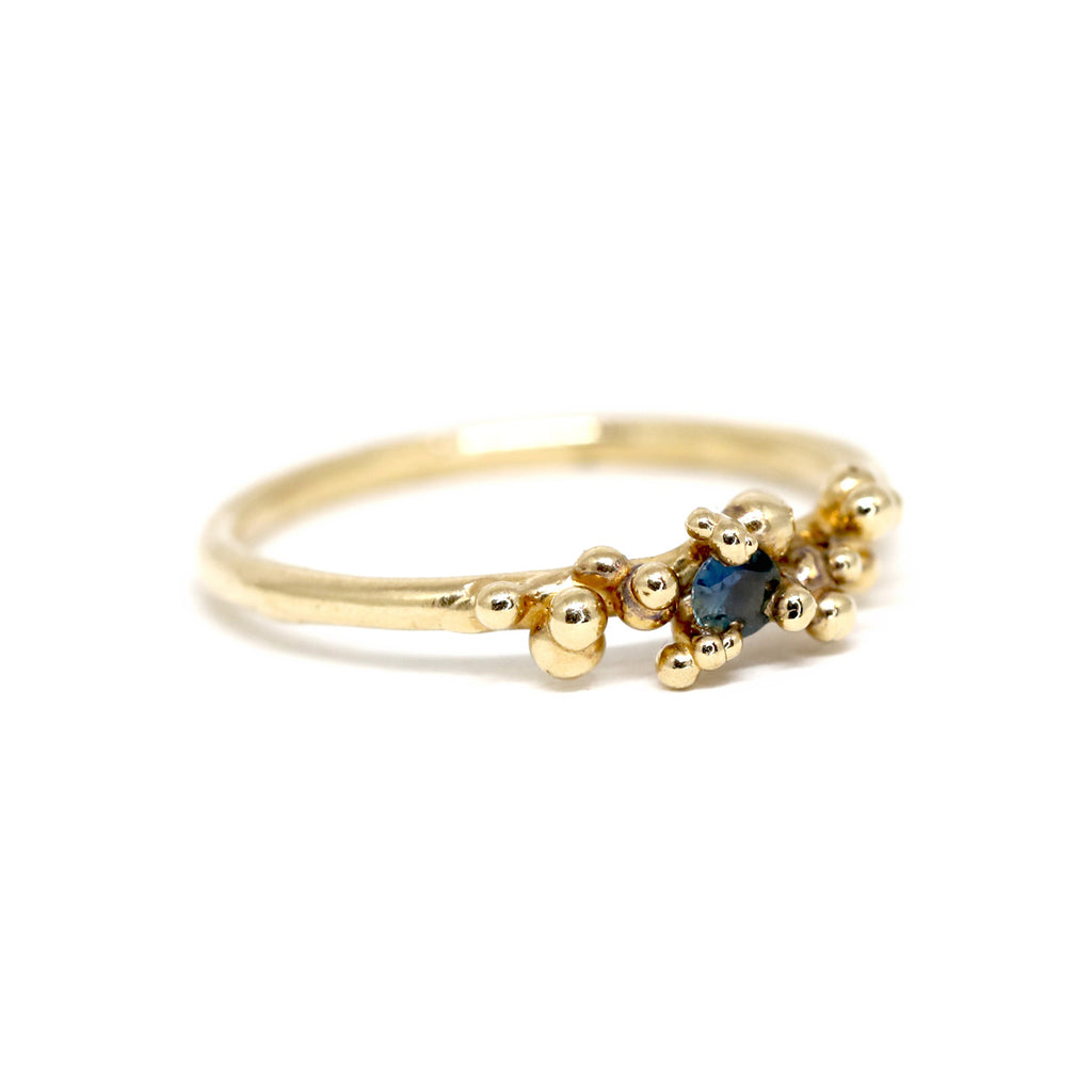 Areia ring on a white background by Toronto-based jewelry designer Meg Lizabet. Organic 14k yellow gold ring with hand-placed gold granules and encapsulated blue sapphire. Unique ring that cannot be reproduced. Find Meg Lizabet's creations in Montreal at Ruby Mardi.