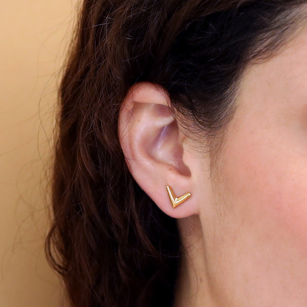 Close up of a simple gold vermeil arrow earring in V shape wear by a girl. Unisex jewelry pieces for parties and for everyday wear. Available online or at our Montreal's Little Italy store, with the work of other jewelry designers. We also offers custom jewelry services in Montreal.