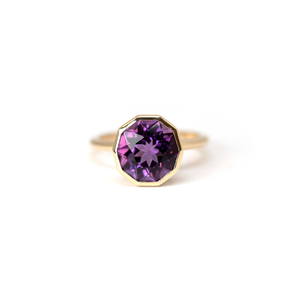 Front view of the splendid statement ring by Bena Jewelry, custom made in Montreal. This fine piece of jewelry is available at the Ruby Mardi jewelry store. Made with a natural gemstone in a deep purple color, this edgy ring is made with an amethyst and set in yellow gold with a bezel setting.