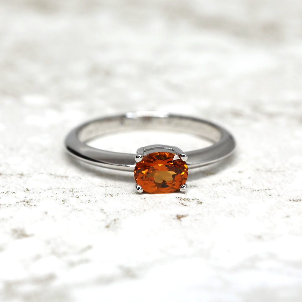 front view of orange garnet gemstone white gold engagement ring made in montreal boutique ruby mardi jeweler in little italy on white textured background