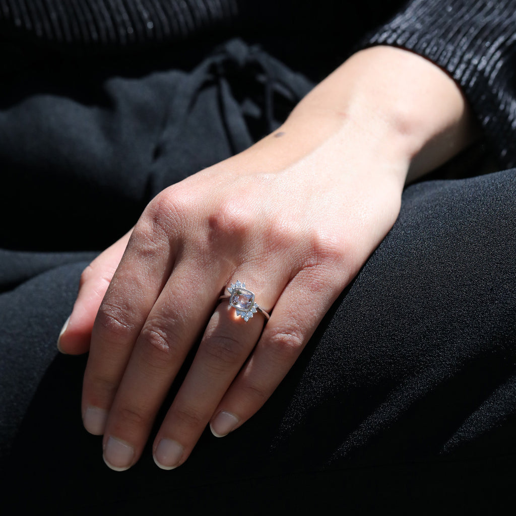 Close up on the hand of a lady dressed in black wearing a luminous engagement ring featuring a cushion natural morganite in an asymmetrical design. This bridal piece of jewelry was handmade in Montreal by Justine Quinal, an independent jeweller represented by Ruby Mardi the only fine jewelry gallery in town. We also offer bespoke services.