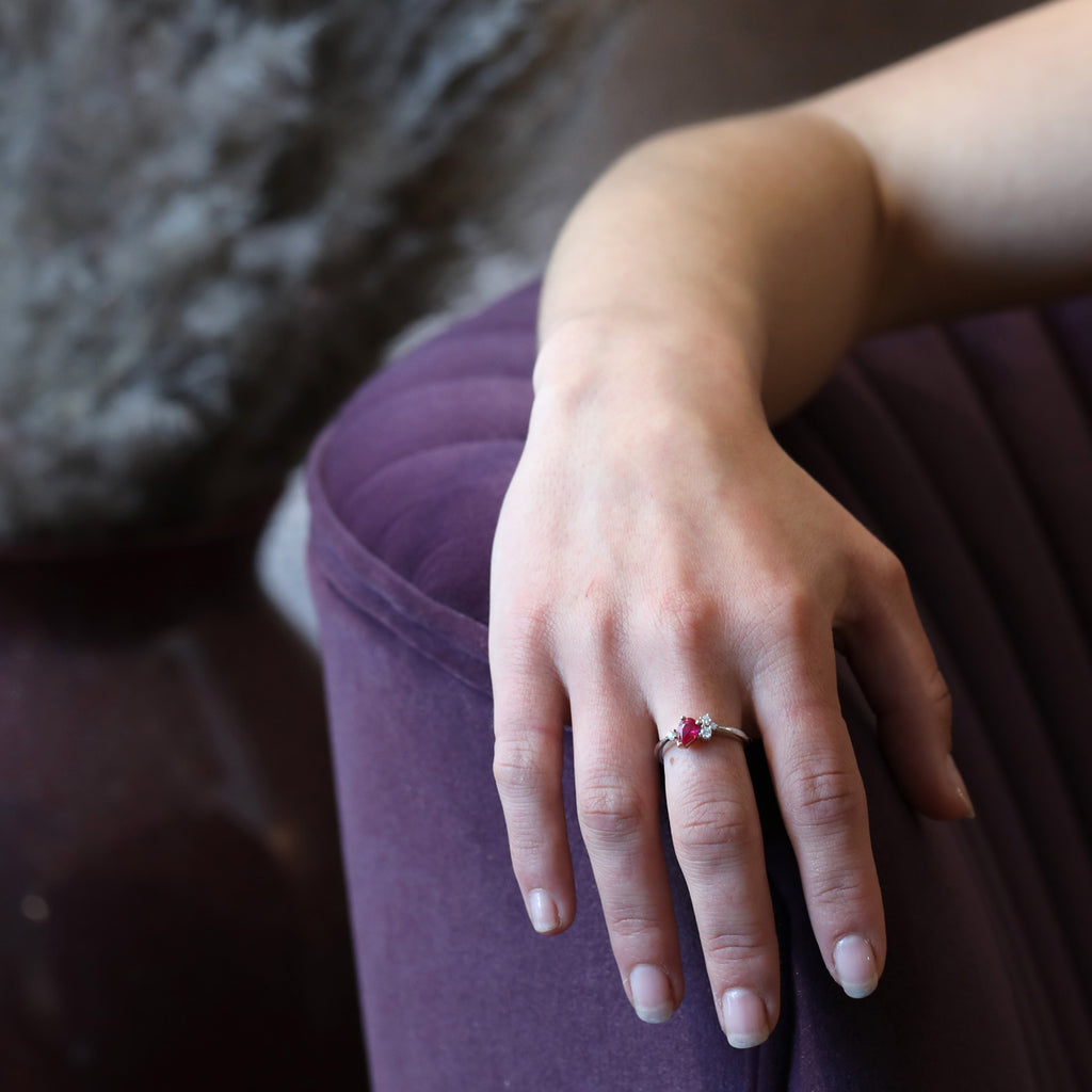 A lady’s hand wearing an engagement ring featuring a pear natural ruby and diamond accents  is placed on a purple sofa. The asymmetrical ring is set in white gold and is a creation from woman jeweller Justine Quintal. Find designer rings at Ruby Mardi, the only fine jewelry gallery and best jewellery store in Montreal.