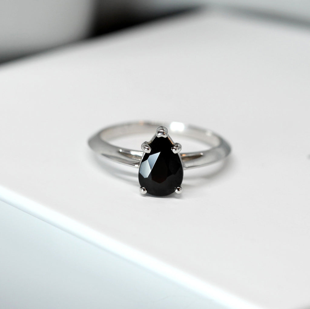 Pear Shape black Spinel Engagement ring on a white background by Ruby Mardi, a fine jewelry gallery in Montreal Little Italy, close by Bijouterie Italienne, and Rosemont, Outremont, Villeray, Parc Extension, Mile End, Mile Ex districts. White gold gemstone ring, bridal jewelry, wedding ring, ethical gem. Ruby Mardi offers custom jewelry services in Montreal. Lab grown diamonds, natural diamonds, Canadian diamonds, ethical diamonds, ethical gemstones.