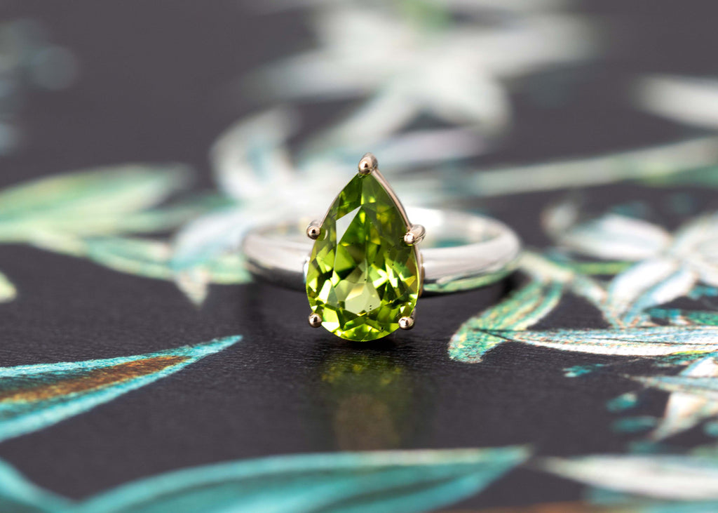 A ring from designer Bena Jewelry seen on a wallpaper. A statement ring featuring a big peridot set in 14 yellow gold with a silver band. Fine jewelry handmade in Montreal and available online for worldwide shipping. 