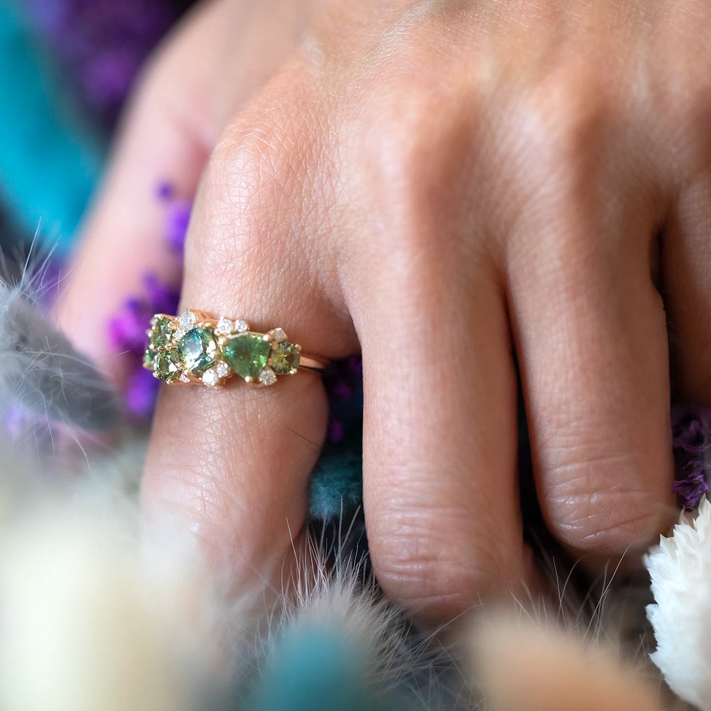 girl wearing a custom avalanche green gemstones made designer bridal ring in yellow gold holding blue and white flowers in montreal