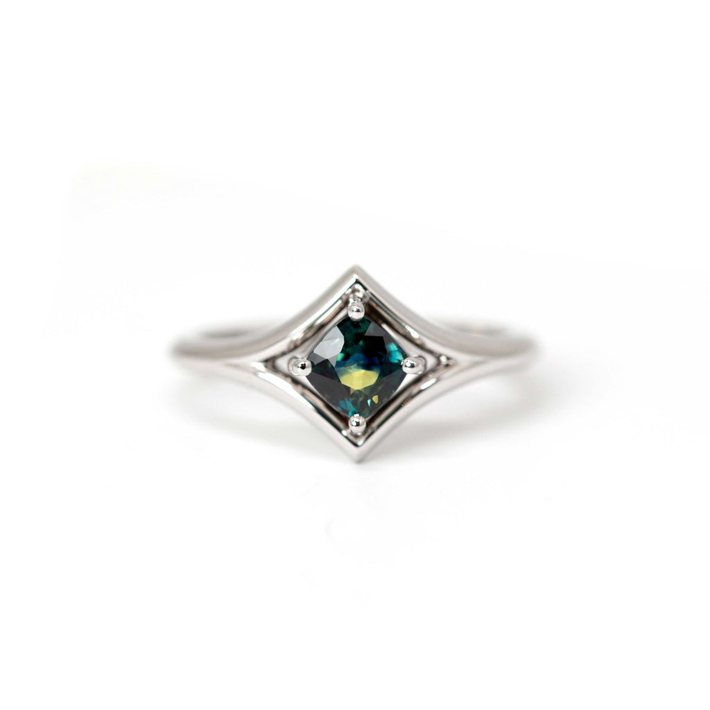 Modern designer ring in white gold with superb sapphire in shades of blue, green and yellow. Set in white gold, this engagement ring is made in Montreal by Canadian jewelry designer Bena Jewelry.