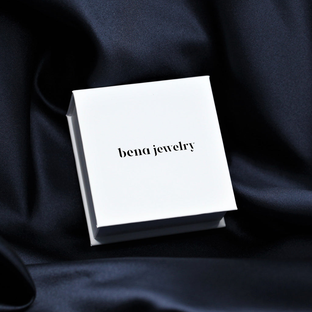 Jewelry packaging of jewellery designer BENA in Montreal. White box with logo photographed on a dark blue fabric.