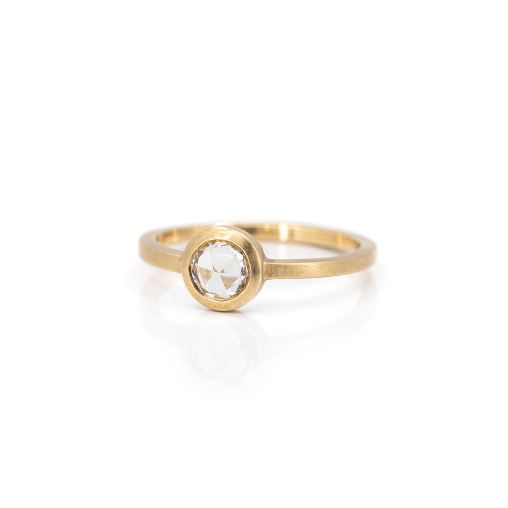 Half side view of a yellow gold alternative solitaire engagement ring with a round rose cut white sapphire, photographed on a white background. One-of-a-kind jewelry piece available at Boutique Ruby Mardi, the best jewellery store in Montreal.
