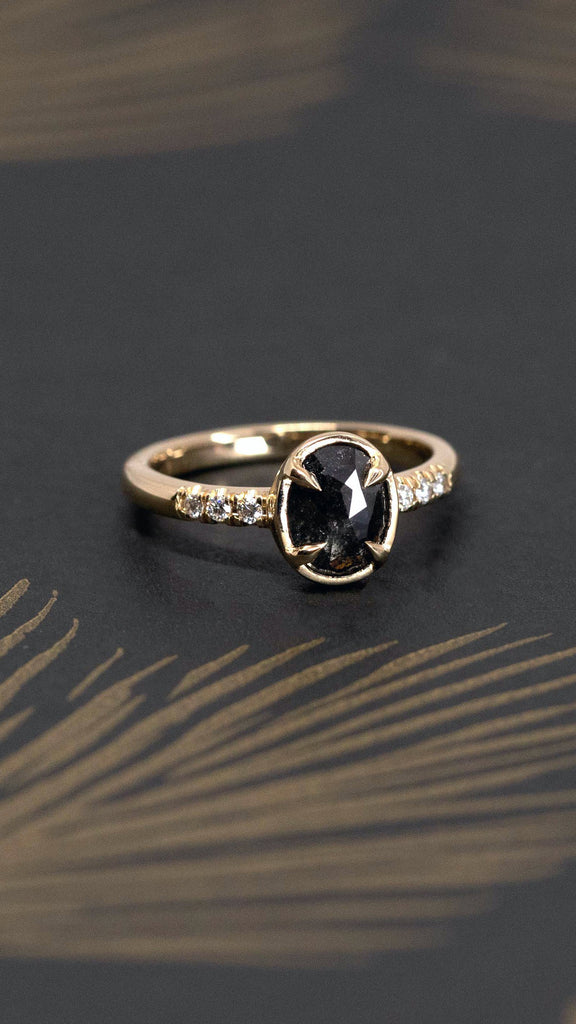 blacj diamond engagement ring custom made in montreal by the designer Yuliya Chorna Jewellery for boutique ruby mardi jeweler in little italy montreal yellow gold ring with small round icy diamond on the side of the band on a dark background