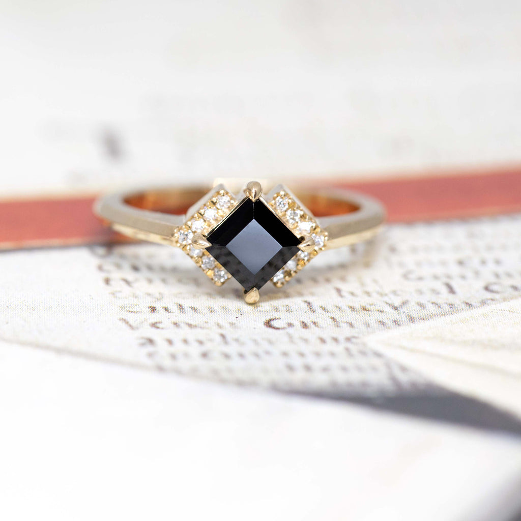 Fine jewelry made by designer Liane Vaz exclusively at Boutique Ruby Mardi jewelry store in Montreal. Edgy engagement ring made with a square shaped black gemstone, a spinel and surrounded by a unique halo made with small round moissonite gems. Yellow gold ring custom made in Canada.