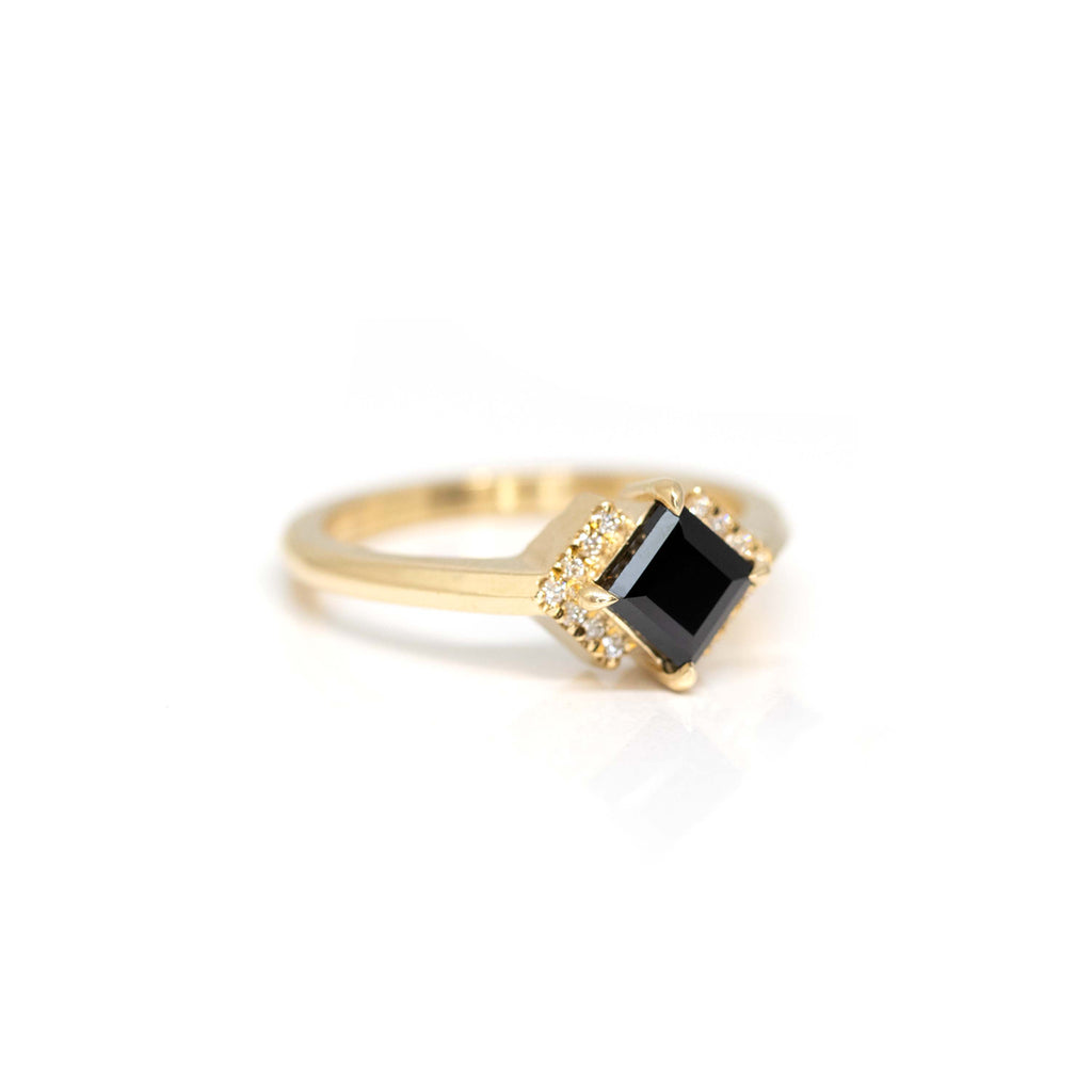 Side view of a yellow gold ring with a square or princess cut black spinel with a round diamond style moissonite halo. This edgy engagement ring is made by jewelry designer Liane Vaz exclusively for fine Montreal jewelry store Ruby Mardi.