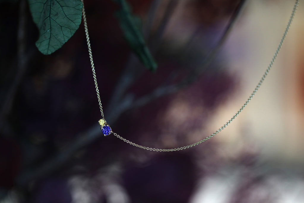 Delicate gemstone necklace featuring yellow and blue sapphire photographed on a romantic flowery background. Available online and at our fine jewelry gallery in Montreal’s Little Italy.