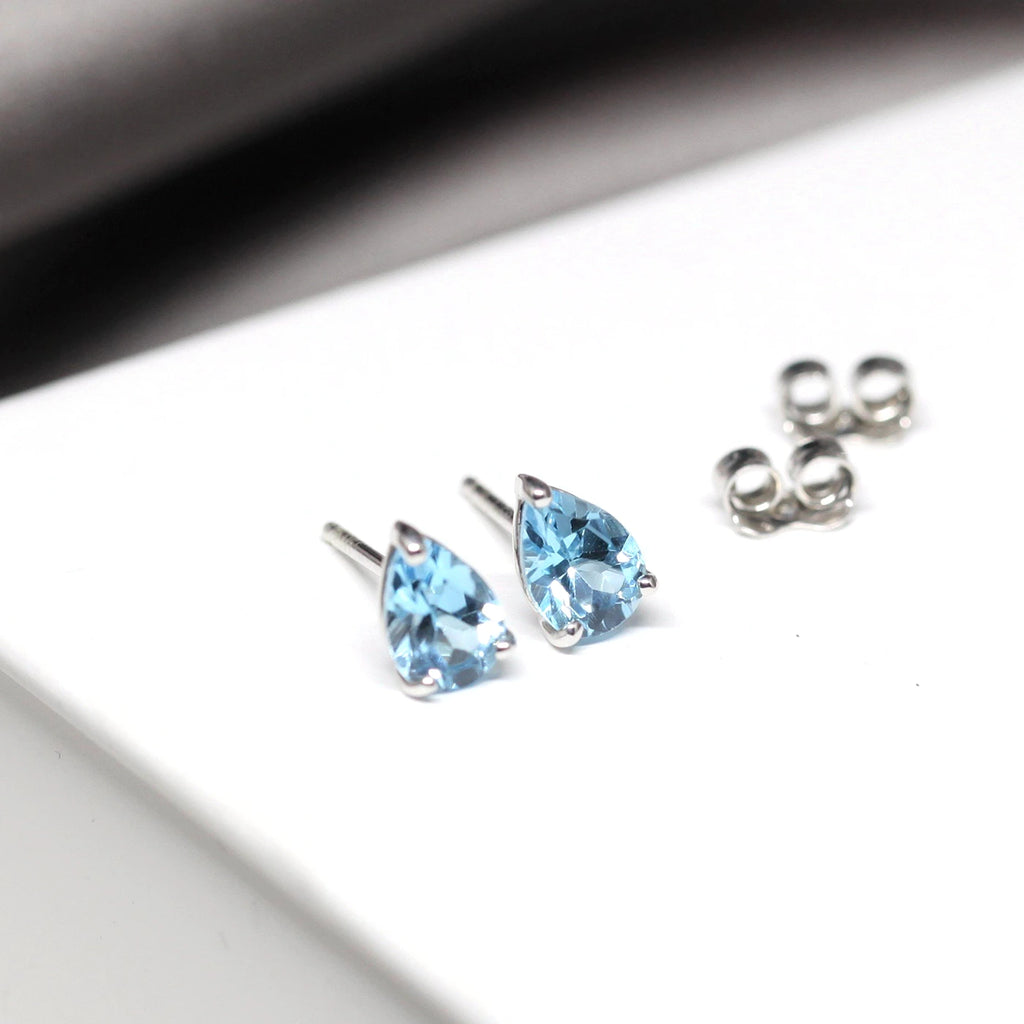 small pear shape gemstone stud earrings minimalist design with sky blue topaz custom made in montreal at the best jewelry in boutique ruby mardi on wite and grey background