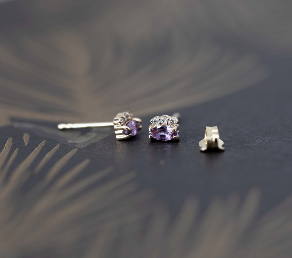 Violet Lilac Sapphire Earrings with 3 diamonds on a white background. Sapphire gemstone stud gold earrings created by Ruby Mardi, a fine jewelry store in Montreal's Little Italy, close by Outremont, Rosemont, Villeray and Mile End districts. We specialize in engagement rings, gold jewelry, heirloom jewelry, bespoke, custom jewelry creation in Montreal. We can source ethical gemstones, natural diamonds, lab grown diamonds, Canadian Diamonds. We sell the work of the most talented Canadian jewelry designers.