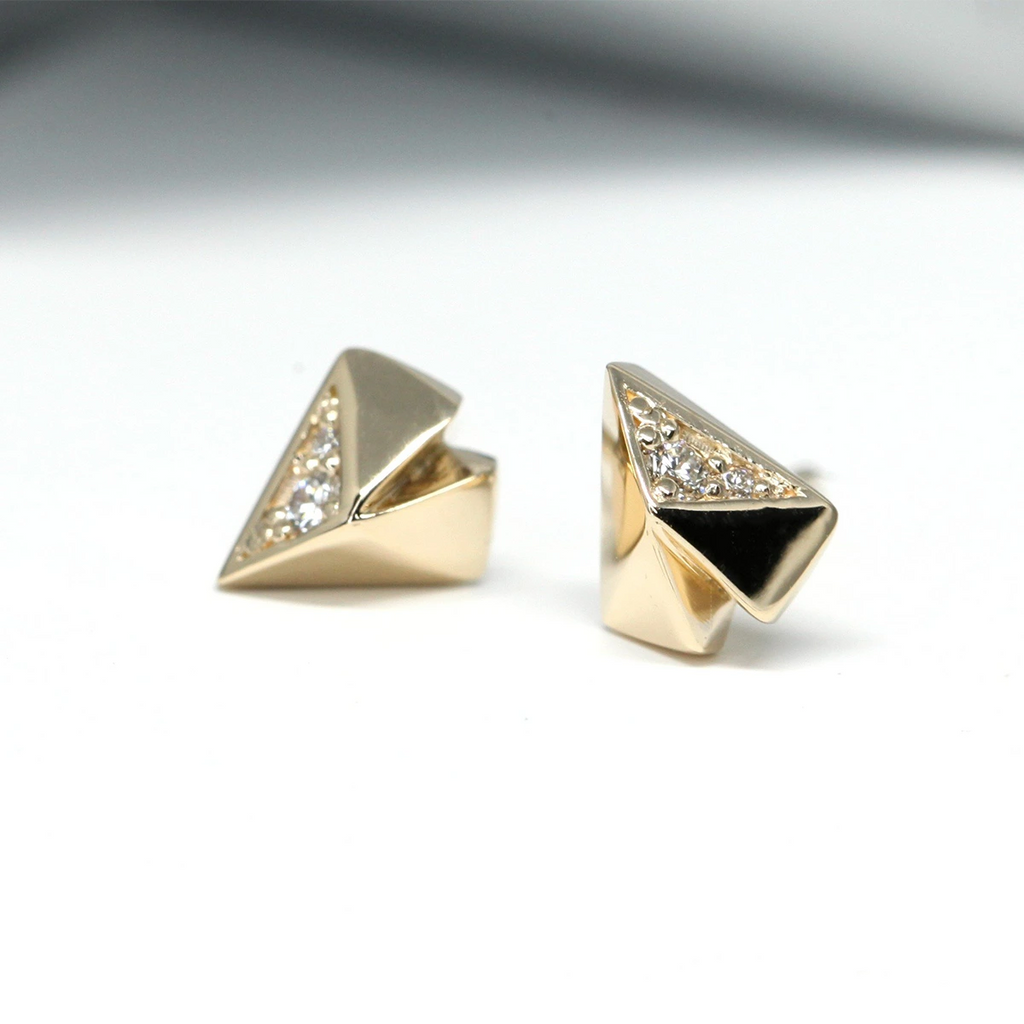 Independent designer gold stud earrings with diamonds seen on a white background, in close up. These earrings are in yellow gold and are in a geometrical heart shape. They can be found at the best jewelry store in Montreal, Ruby Mardi.