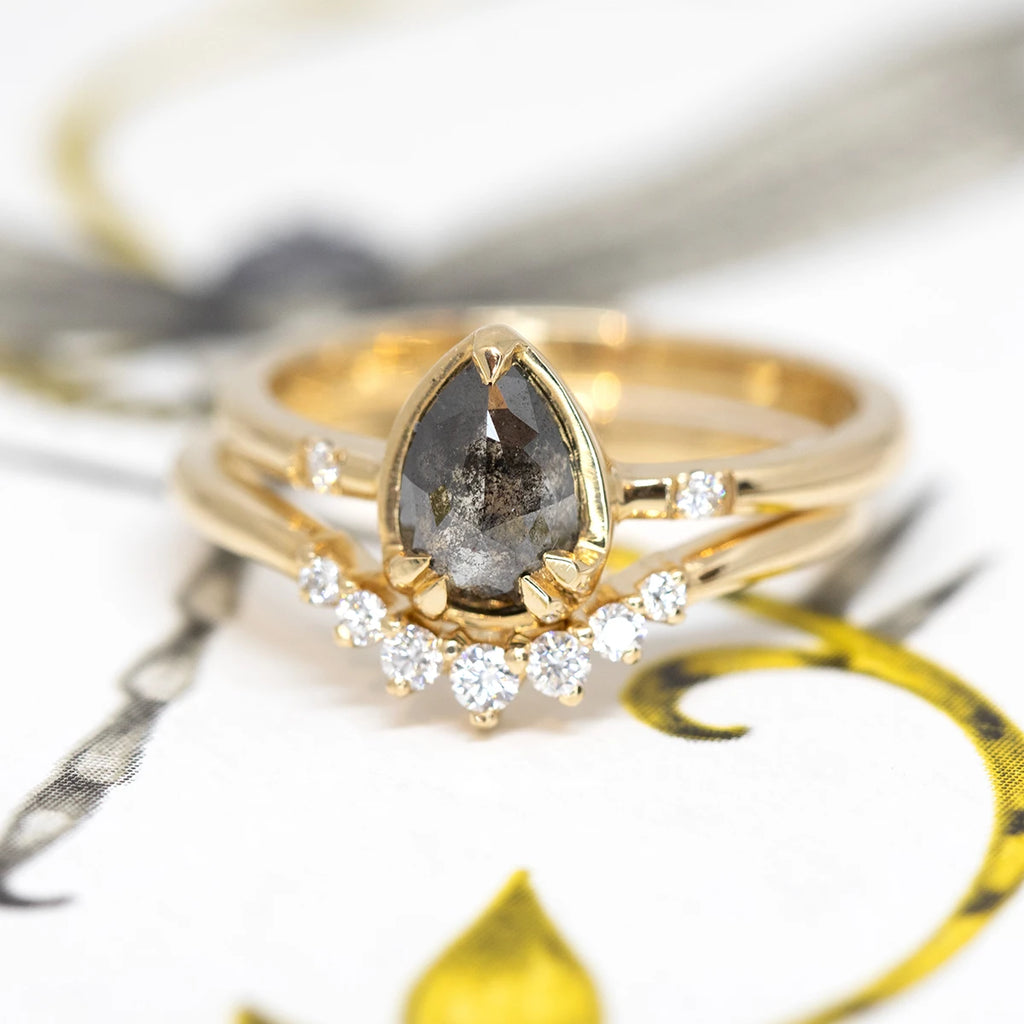 Two beautiful rings by designer Yuliya Chorna are photographed up close. You can see the details of the salt-and-pepper diamond inclusions in the yellow gold engagement ring. The matching wedding band shows a gradation of diamonds. 