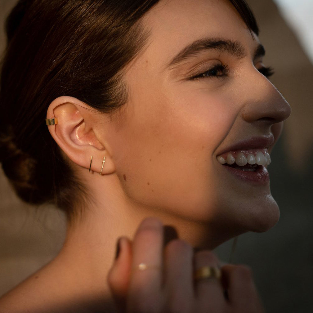 Delicate dainty 18k yellow gold designer earrings worn by a young laughing lady.