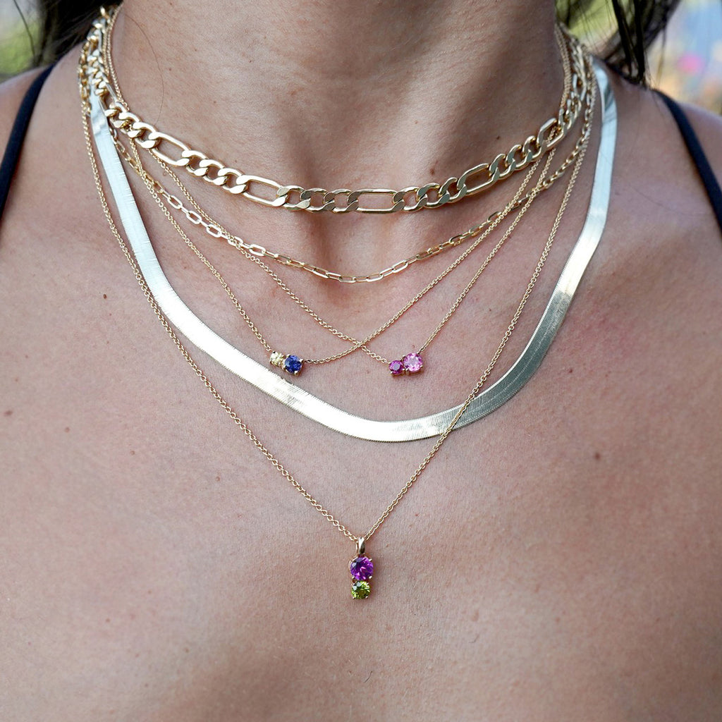 Plusieurs chaînes, colliers et pendentifs en or dans le cou d'une femme. Bijoux avec pierres précieuses et autres bijoux fins disponibles à la bijouterie Ruby Mardi, dans la Petite Italie de Montréal.