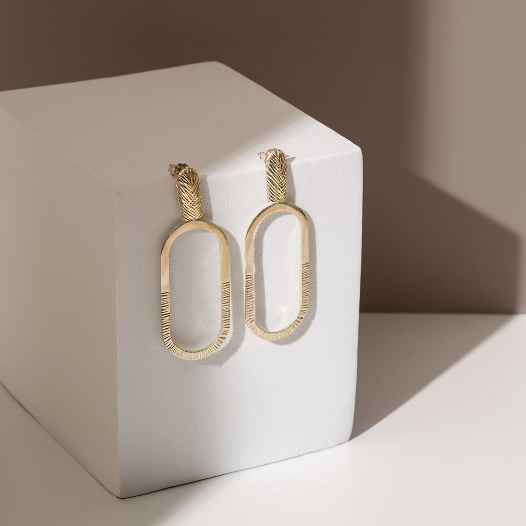 Beautiful textured big hoop earring in gold vermeil seen photographed over a white cube. 