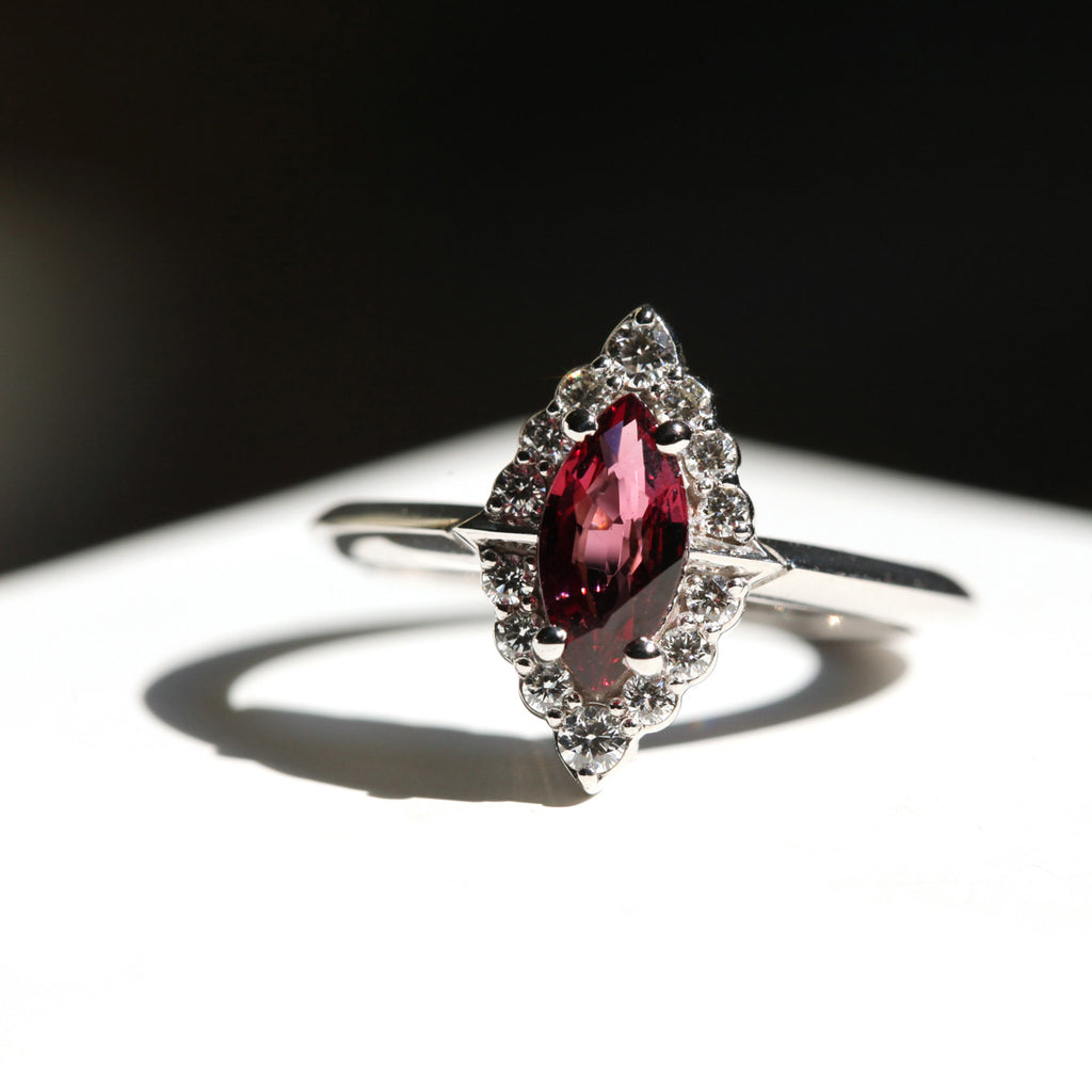 Artistic light and shade photography of a lovely engagement ring featuring raspberry-red garnet with a halo of round brilliant natural diamonds. This 14k white gold ring is available online or at our Montreal jewelry store.