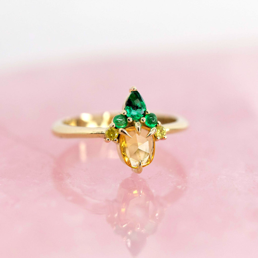 A beautiful jewelry creation featuring yellow sapphire, emerald and diamonds. This engagement ring or right hand ring is photographed on a quartz rose background.